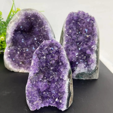 Three purple amethyst geodes on a dark surface with a white background
