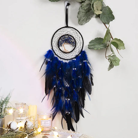 Decorative dreamcatcher with blue and black feathers hanging on a white wall with greenery.