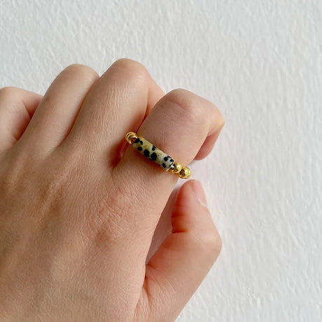 Hand wearing a gold ring with black and white pattern on a plain background