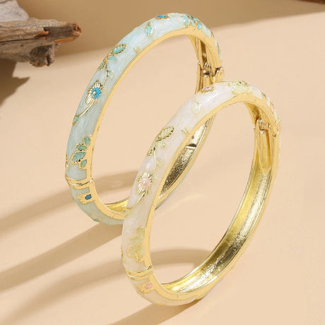 Two gold-rimmed bangles with floral patterns on a beige background