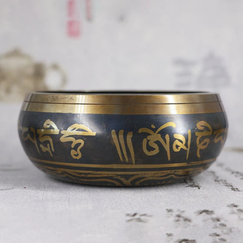 Black singing bowl with gold script on a textured surface
