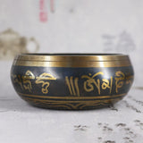 Black singing bowl with gold script on a textured surface