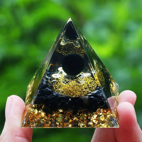 Pyramid-shaped crystal with gold and black interior held by a hand against a green blurred background