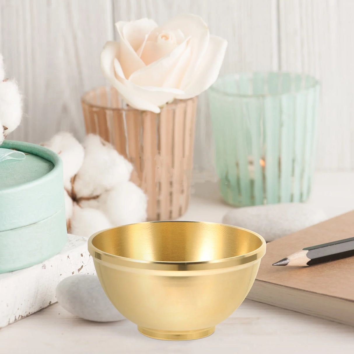 Gold bowl on a surface with decorative items including a rose and candles.