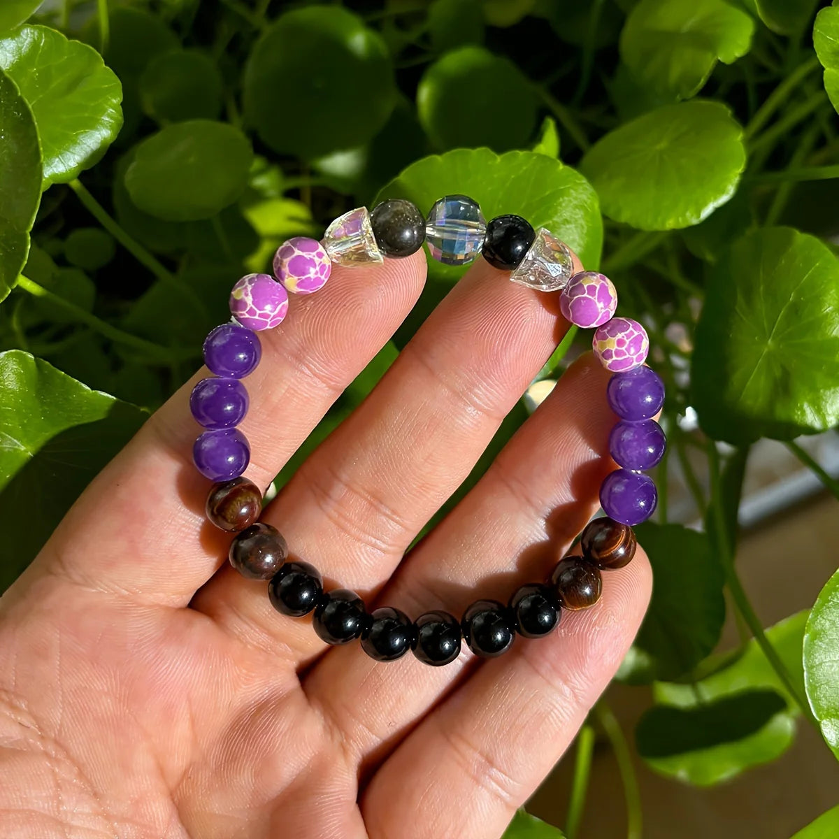 Beaded bracelet with purple, black, and clear beads held in a hand against a green leafy background