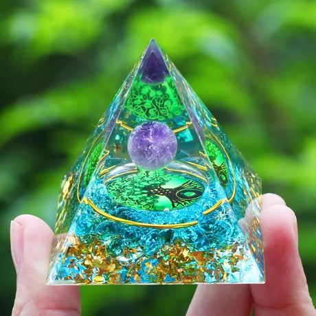 Crystal pyramid with purple and green elements held in a hand against a blurred green background