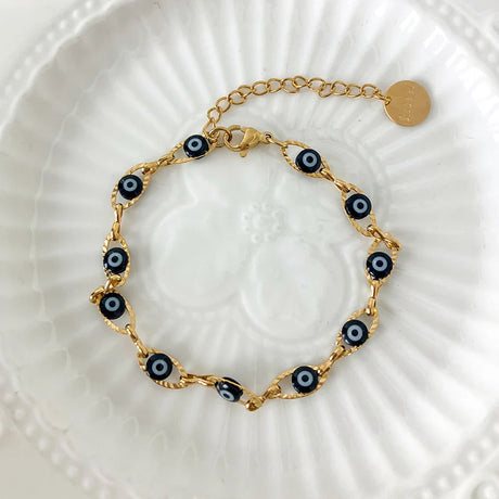 Gold bracelet with black evil eye charms on a white textured surface