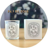 FEU DE BOIS candle and packaging on a wooden surface with a blurred floral background
