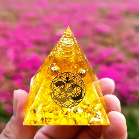 Triangular yellow crystal with a symbol held in front of a pink flower field
