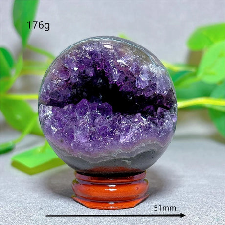 Amethyst crystal sphere on a stand with green leaves in the background