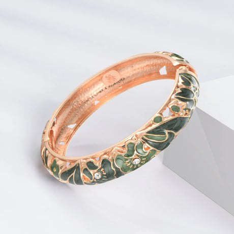 Rose gold bracelet with green enamel and gemstones on a light gray background