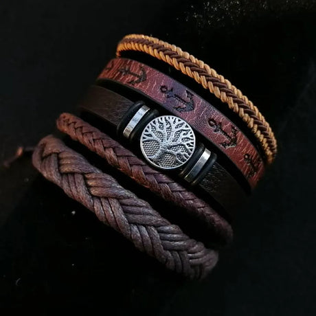 Stack of braided leather bracelets with a central silver tree-of-life charm on a dark background