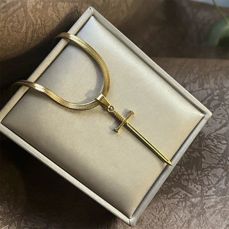 Gold necklace with a sword pendant on a beige box