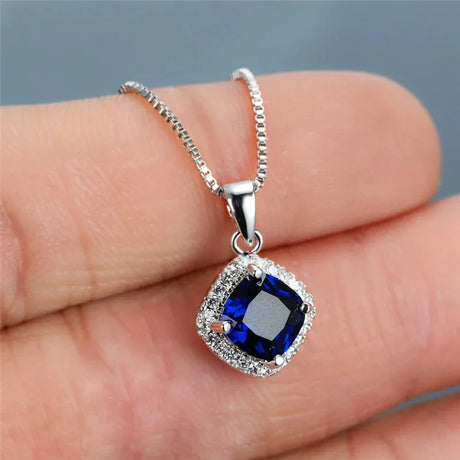 Silver necklace with a blue gemstone pendant held on a hand against a gray background