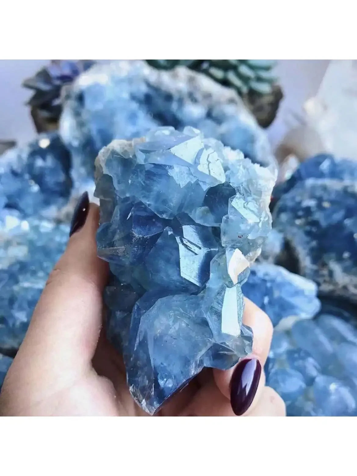 Hand holding a large blue crystal with more crystals in the background