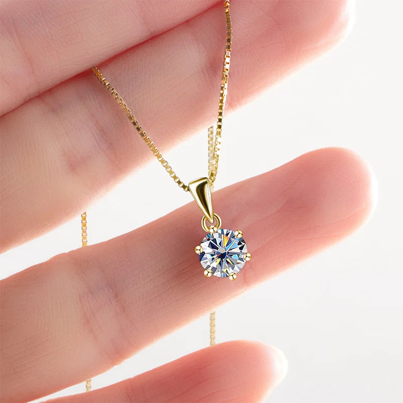Gold necklace with a diamond pendant held between fingers against a white background