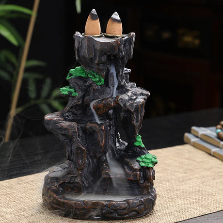 Decorative incense burner shaped like a mountain with two incense sticks on top.