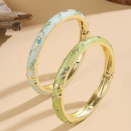 Two gold-rimmed bangles with green and blue patterns on a beige background