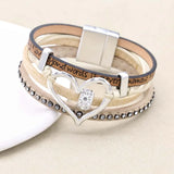 Stack of layered bracelets with a heart-shaped clasp on a beige background