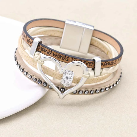 Stack of layered bracelets with a heart-shaped clasp on a beige background
