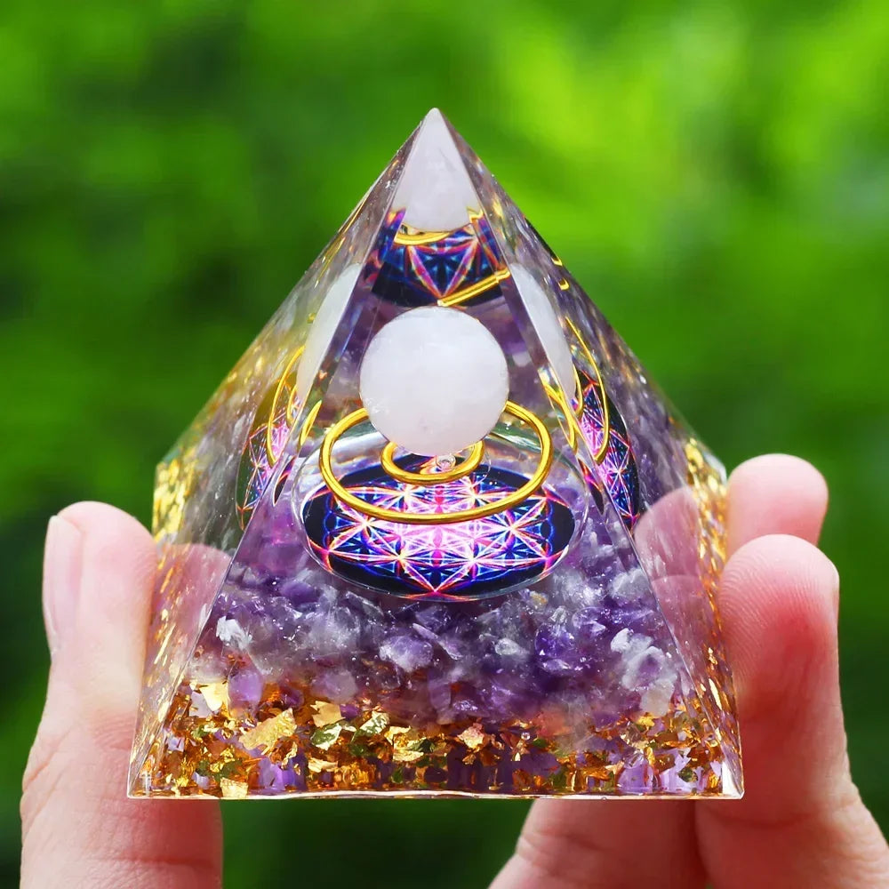 Pyramid-shaped crystal with colorful design held by a hand against a green blurred background