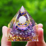 Pyramid-shaped crystal with colorful design held by a hand against a green blurred background