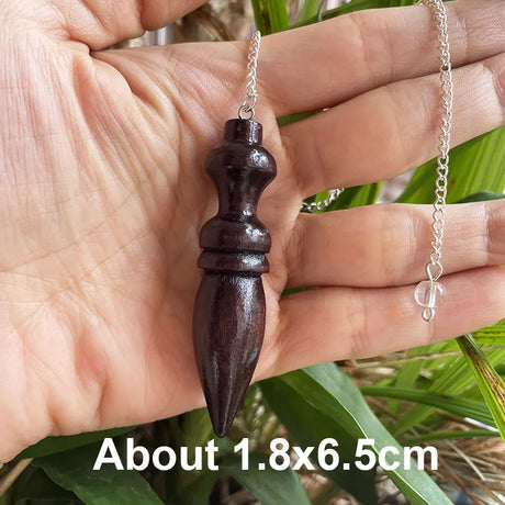 Wooden pendant on a chain held in a hand with green leaves in the background