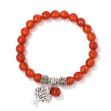 Bracelet with red beads and a silver tree charm on a white background