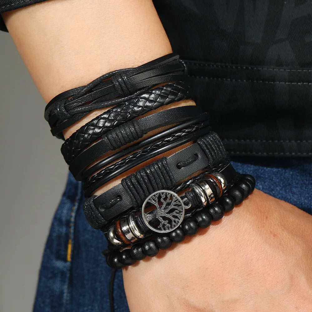 Multiple black leather bracelets on a wrist with a tree of life charm.