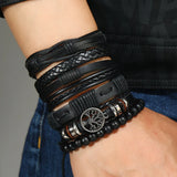 Multiple black leather bracelets on a wrist with a tree of life charm.