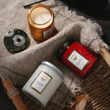 Two candles and a bottle of perfume on a textured surface with a soft focus background.