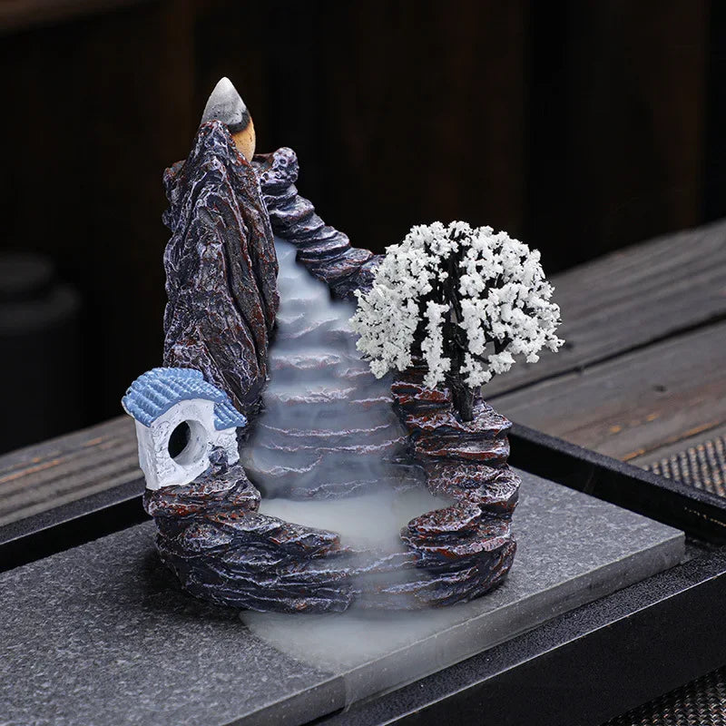 Decorative fountain with rocks, tree, and small house on a dark surface
