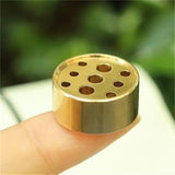 Gold-colored metal component with holes held between fingers against a blurred green background