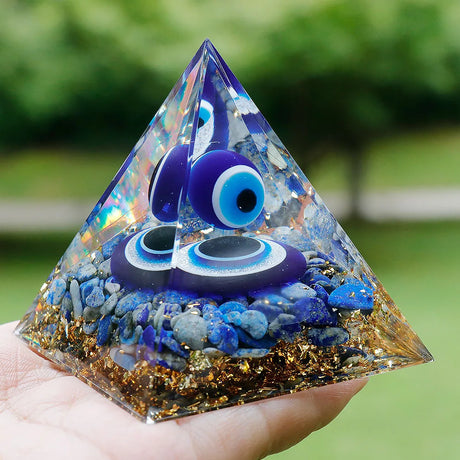 Pyramid-shaped object with blue eyes and stones held in a hand outdoors