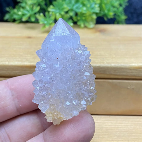 Crystal rock held in a hand with a wooden surface and greenery in the background