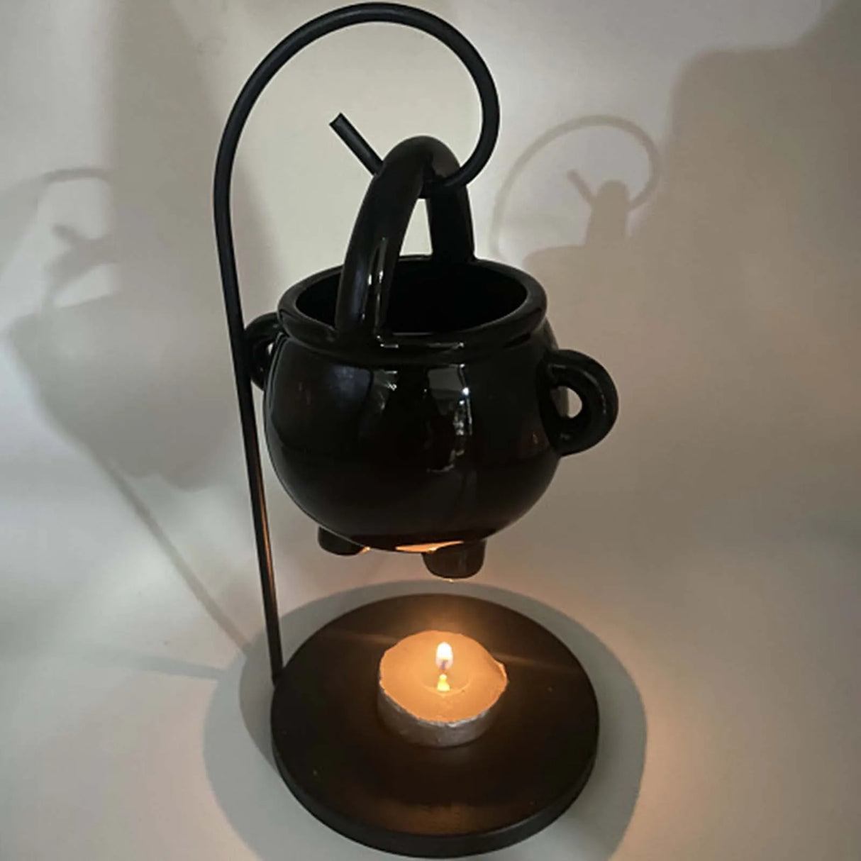 Black ceramic oil burner with a lit candle on a white background