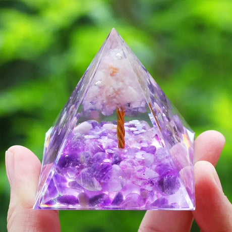 Pyramid-shaped crystal with purple and white stones held by a hand against a green blurred background