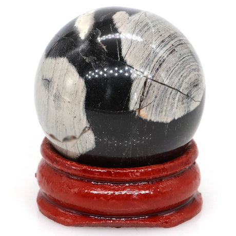 Polished black and white stone sphere on a red stand against a white background