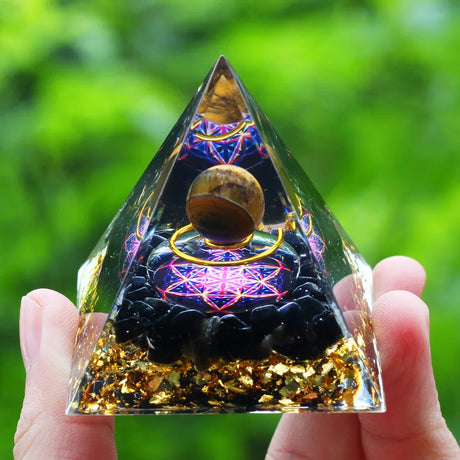 Pyramid-shaped crystal with intricate designs held in a hand against a green blurred background