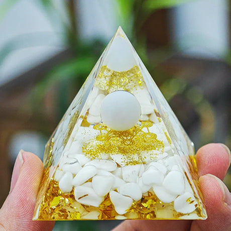 Triangular pyramid with white stones and gold flakes held by a hand against a blurred natural background