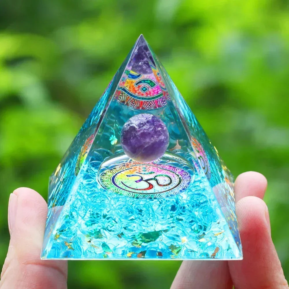 Pyramid-shaped crystal with colorful designs and a purple sphere, held against a green blurred background.