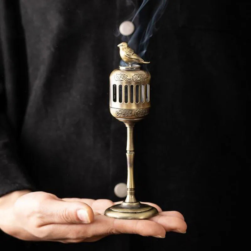Brass incense burner with bird design held by a person against a black background