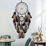 Large dreamcatcher with feathers hanging on a wall in a room with a table and decorative items.