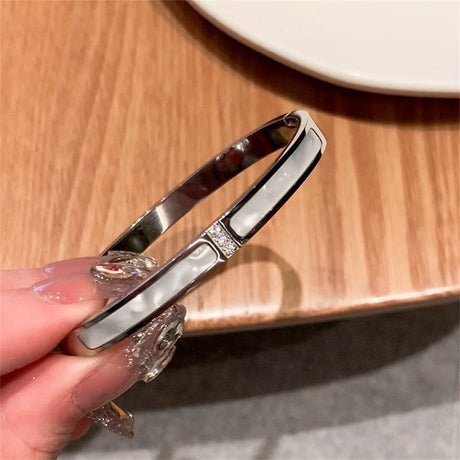 Silver bracelet with decorative elements held by a hand on a wooden surface.
