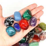 Hand holding a variety of colorful gemstones on a white background