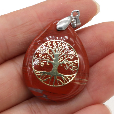Red stone pendant with tree of life design held in a hand