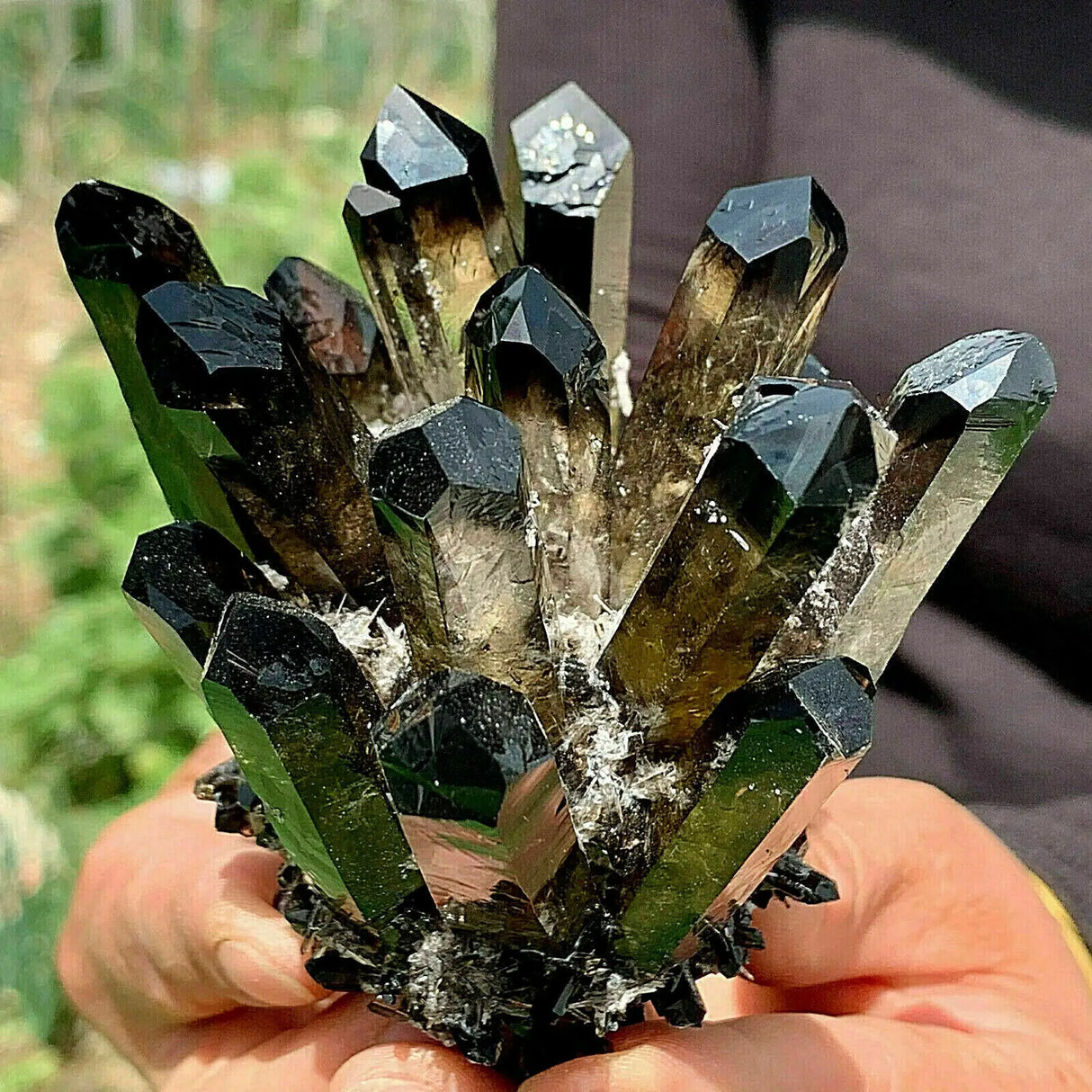 Close-up of a hand holding a cluster of green and black crystals.