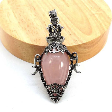 Pink stone pendant with silver decorative elements on a wooden block