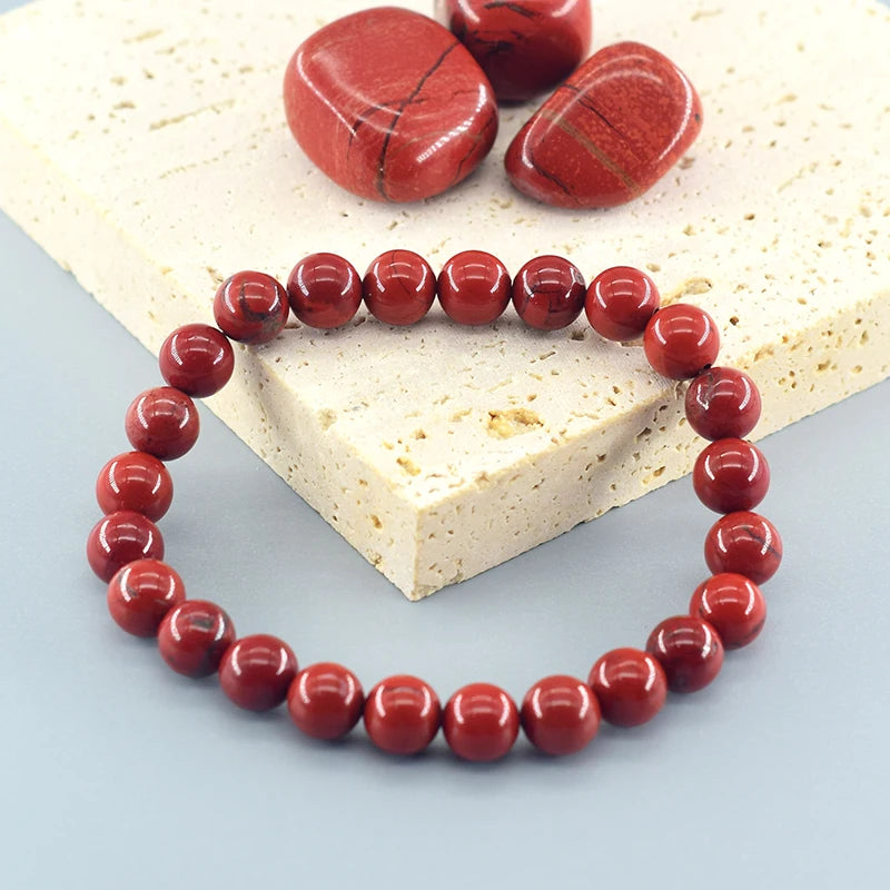 Red beaded bracelet on a light blue surface with red stones on a beige stone background