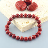 Red beaded bracelet on a light blue surface with red stones on a beige stone background